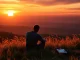Person reflecting on coping with grief while watching a sunset over the hills.